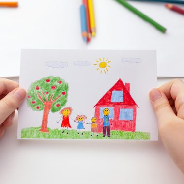 Child holding a drawing with a happy family and an apple tree and a house